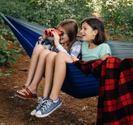 Two kids sitting in hammock holding binoculars.