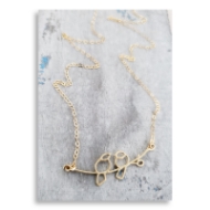 Gold love bird necklace featuring two birds sitting across branch. In front of white and grey background. 