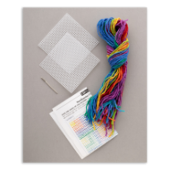 Contents of the needlepoint coaster set: two square plastic grids, a needle, instruction sheet, and colorful strands of yarn.