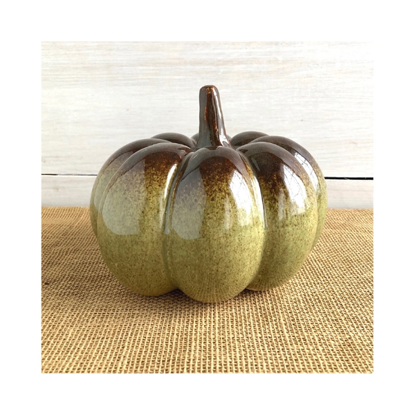 Shiney, sage green, stoneware pumpkin in bright window light resting on burlap. 