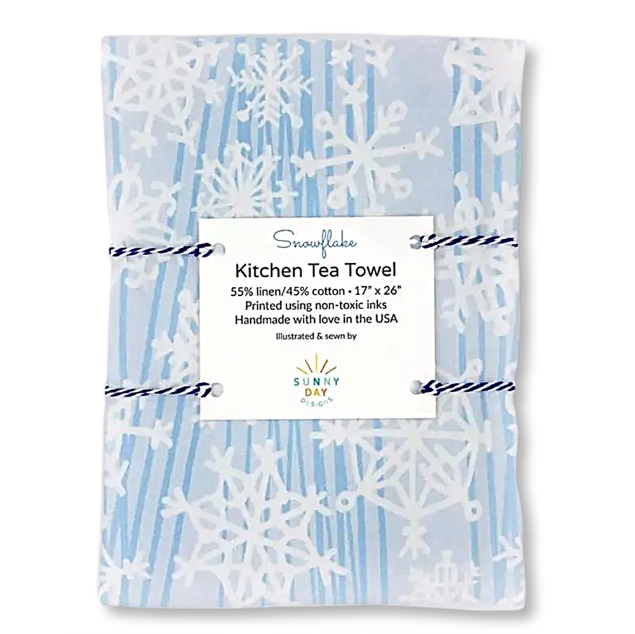 Light blue and white tea towel with a snowflake print design. It is folded into a rectangle and bundled with string. 