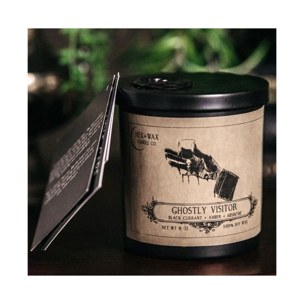 "Ghostly Visitor" candle from Hex + Wax Candle Company. Dark glass container, black metal lid, tan paper label.