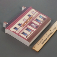 Product photo, side angle, of the miniature wood cutout of Old World Wisconsin's Four Mile House. A ruler shows a width of 5.5 inches.